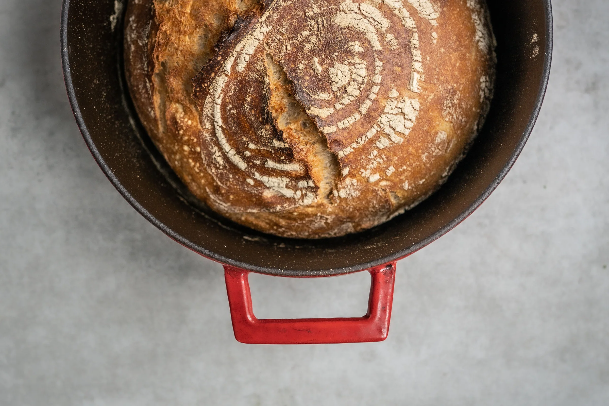 Frisch gebackenes rustikales Brot mit knuspriger Kruste in einem roten gusseisernen Topf